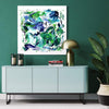Vibrant abstract painting | Emerald Whirlwind 100x100cm
Large contemporary abstract artwork with bold green, blue, and white brushstrokes displayed on a modern gray cabinet against a teal wall, accented by lush foliage and metallic decor.