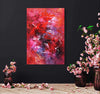 Vibrant abstract artwork in reds and pinks with splashes of color, displayed on a dark wall surrounded by vases of pink cherry blossoms.