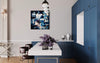 Large abstract painting of blue and white shapes hanging on the wall in a modern kitchen with navy blue cabinets and a white countertop. The room is furnished with contemporary decor including a metal table and chairs.