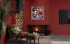 Vibrant abstract art piece on warm red wall above fireplace, surrounded by wooden logs and cozy furniture, creating a modern and inviting living space.