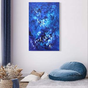 Large abstract blue canvas art titled "Can't Stay Away" displayed on the wall of a cozy living room setting with a blue floor cushion and decorative elements.