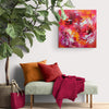 Vibrant abstract art on canvas: Colorful, expressive painting with bold brushstrokes and a dynamic composition displayed on a white wall above a cozy seating area with throw pillows and blanket.