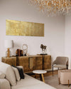 Elegant modern living room with large golden abstract artwork, wooden sideboard, and ornate crystal chandelier overhead.