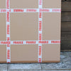 Fragile boxes stacked against a wooden wall, with prominent "FRAGILE" warning labels on the packaging.