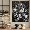 Dramatic black and white abstract canvas artwork with bold brushstrokes, displayed in a modern interior setting with a wicker chair and decorative accessories.
