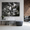 Abstract black and white painting depicting bold, dynamic brushstrokes on a large canvas displayed in a modern living room setting.