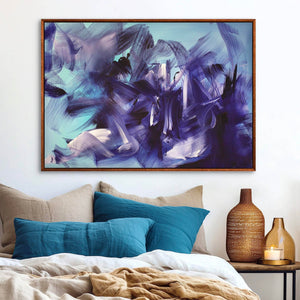 Vibrant abstract landscape artwork titled "Echoes In Blue" featuring a dynamic blend of blues, purples, and brushstrokes, displayed in a wooden frame and hanging above a cozy bedroom setting with plush bedding and decor.