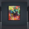 Vibrant abstract painting in colorful earthy tones of red, green, yellow, and blue displayed on a dark wall