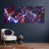 Vibrant abstract art canvas with rich colors and bold brushstrokes, displayed prominently on a dark wall in a modern living space with a comfortable chair and side table.
