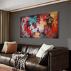 Extra large abstract landscape canvas art with vibrant red, blue, and earthy brown tones, displayed on the wall above a brown leather sofa in a modern living room setting.