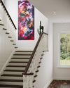 Vibrant abstract landscape painting in modern stairwell. Colorful floral-inspired artwork with bold brushstrokes and warm hues. Large vertical canvas art piece displayed prominently on the wall, complementing the wooden staircase and neutral decor.