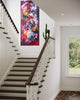 Vibrant abstract landscape painting in modern stairwell. Colorful floral-inspired artwork with bold brushstrokes and warm hues. Large vertical canvas art piece displayed prominently on the wall, complementing the wooden staircase and neutral decor.