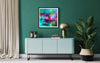 "Vibrant Abstract Art Print" - Framed colorful abstract painting with bold, expressive brushstrokes hanging on a green wall above a modern grey sideboard, complemented by lush greenery and minimal decor elements in a contemporary interior setting.