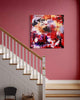 Vibrant abstract artwork on display in a modern staircase setting. The large square canvas features a bold, colorful abstract composition with swirling brushstrokes and a mix of warm and cool tones. The artwork's placement in the stairwell creates an eye-catching focal point and adds a touch of contemporary style to the space.