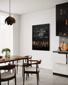 Minimalist black and white abstract painting displayed in a modern dining room setting with a wooden dining table, dark chairs, and a unique light fixture.