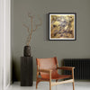Framed "Golden Idol" Signed Edition Art Print displayed on gray wall, with a wooden chair and ornamental branches in a vase nearby, creating a modern and abstract interior design setting.