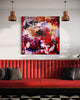Vibrant abstract art painting on the wall of a modern living room, with a red leather sofa and checkered floor below it. Warm copper pendant lights illuminate the space.