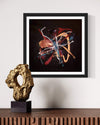"Chameleon" Signed Edition Abstract Art Print - Vibrant, dynamic abstract artwork featuring bold colors and organic shapes on a dark background, displayed in a black frame on a wooden shelf with a gold sculpture.