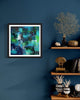 "Vibrant Abstract Art Print" - Framed modern abstract artwork featuring a colorful, expressive composition in teal, green, and blue hues displayed on a deep teal wall. Surrounding shelves showcase decorative elements like coral, vases, and books, creating an elegant, artistic interior setting.