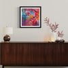 Vibrant abstract art print "Falling In Love I" by Paresh Nrshinga displayed on the wall above a wooden cabinet with decorative elements including a lamp, branches, and pinecones.