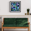 Colorful abstract art print titled "Under The Waves" displayed in a modern living room setting. The artwork features a vibrant mix of blues, greens, and black brushstrokes, creating a sense of depth and movement. The framed print is hung on a white wall, complementing the neutral-toned decor and wooden furniture in the room.