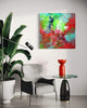 Vibrant abstract painting on canvas displayed in a modern home interior with a grey armchair, a red vase, and a potted plant.