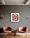 "Vibrant Abstract Art" - Framed print featuring bold brushstrokes and a striking color palette, displayed on a gray wall between two modern coral-colored armchairs and a wooden side table in a stylish interior setting.