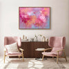 Vibrant abstract canvas art depicting colorful dancing petals in pink, purple, and orange tones, displayed on the wall of a modern living room setting with plush pink armchairs and a wooden sideboard.