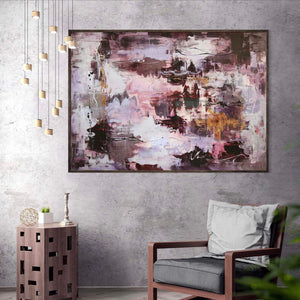 Large abstract canvas art depicting an earthy, modern landscape with bold, colorful brushstrokes. Displayed in a contemporary living room setting with a wooden side table and cozy armchair.