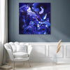 Large blue abstract canvas painting with swirling, fluid shapes and vibrant hues displayed on a wall in a modern, minimalist living room setting.