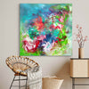 Vibrant abstract painting with colorful brushstrokes and splashes of turquoise, green, pink, and red hues, displayed on a wall in a modern home setting with natural decor elements.