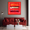 Vibrant abstract art on canvas with bold red and gold tones, framed and displayed on a gray wall above a red velvet sofa in a modern living room setting.