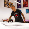 Large abstract paintings in vibrant colors and textures on the walls, man in Converse shirt working on a new abstract artwork on a canvas, art supplies and tools on the table, creative and artistic workspace.