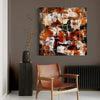 Vibrant abstract artwork | Large square canvas with fiery orange, black, and white brushstrokes | Displayed above a wooden armchair in a modern interior setting