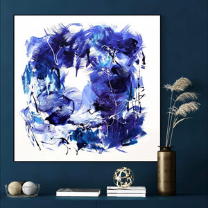 Large abstract blue and white canvas art titled "Reach For The Sky" showcasing a vibrant, expressive painting with fluid brushstrokes and splashes of color. Displayed in a modern setting with books, decor, and natural elements, the artwork adds a striking visual focal point to the room.