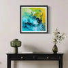 Vibrant abstract art print "Spring Morning" by Paresh Nrshinga displayed on a wall above a dark wooden table with decor items.